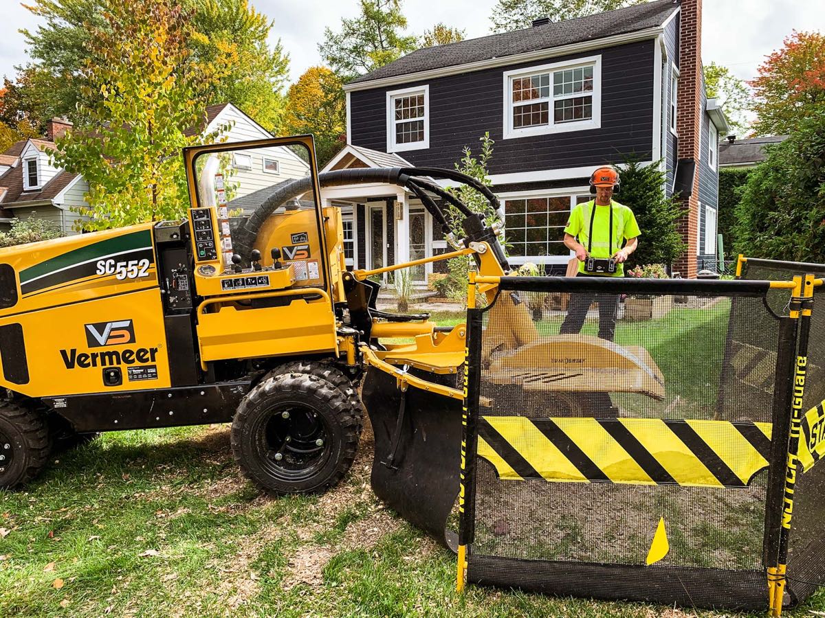 An operator running a stump grinder on a front lawn
